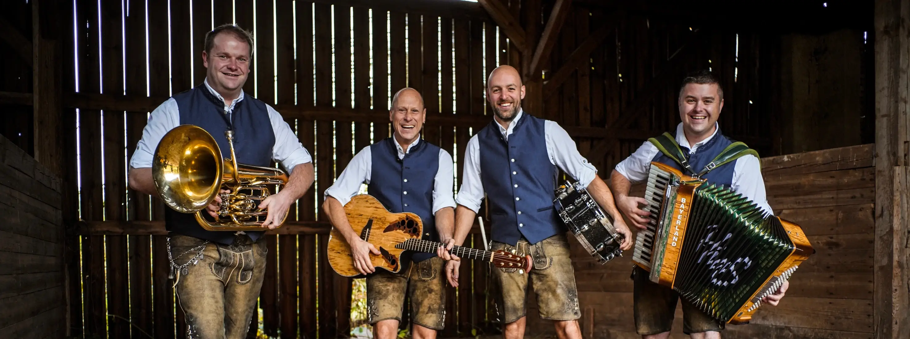 Breznsalzer – die bayrische Partyband aus Schwandorf, vier Musiker in Tracht mit Tuba, Gitarre, Trommel und Akkordeon in rustikaler Scheune.