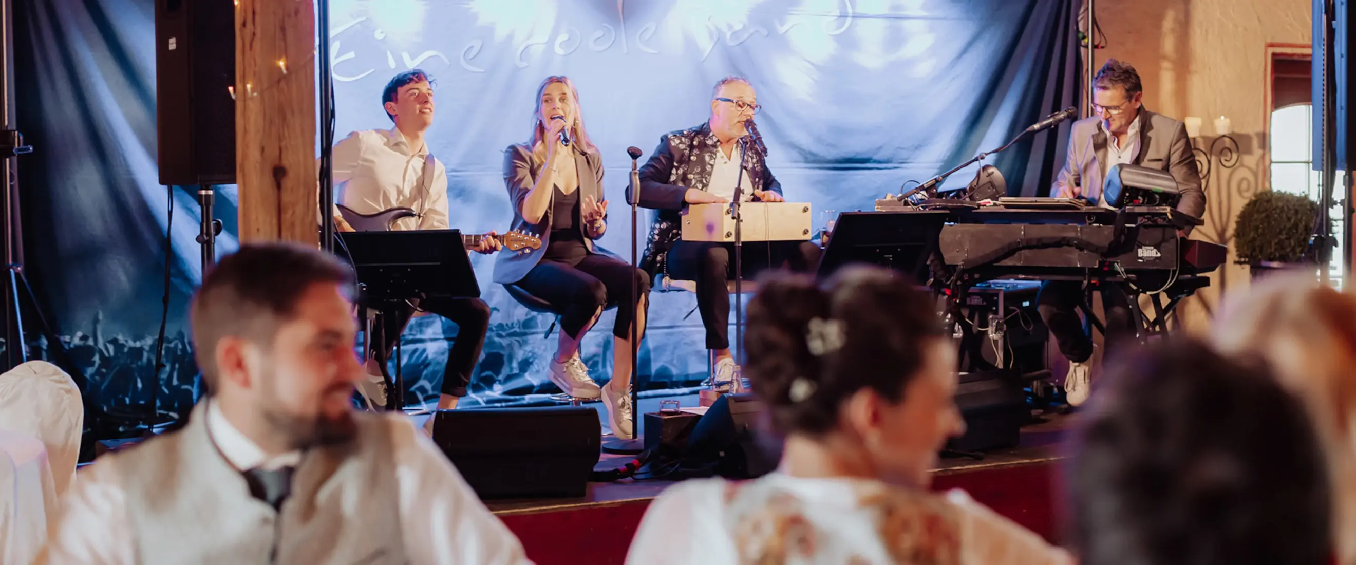 James Band – die Partyband aus Rosenheim live auf einer Hochzeit, mit Sängerin, Gitarrist, Keyboarder und Percussionist auf festlich beleuchteter Bühne.