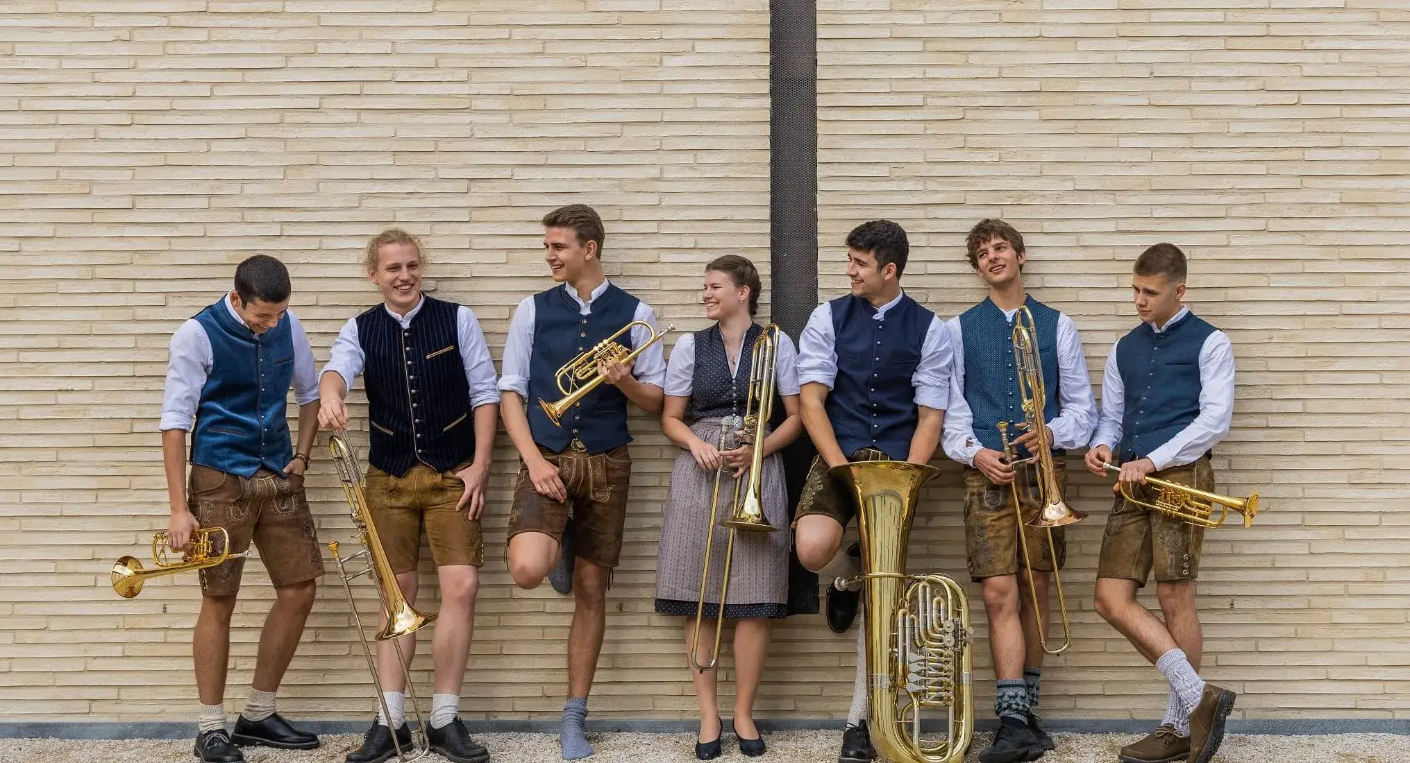 Die Musiker der Blaskapelle Blechhilfswerk lehnen mit dem Rücken an eine Wand und halten dabei ihre Instrumente in ihren Händen.