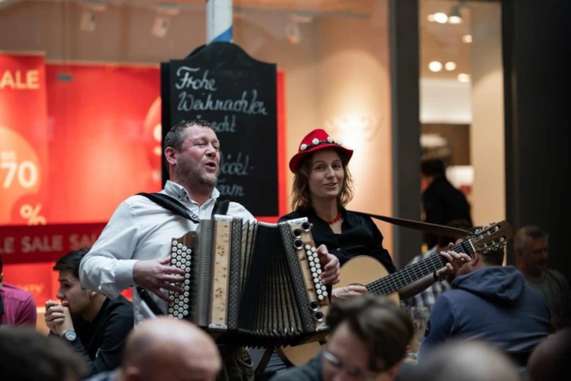 Die beiden Musiker des Duo`s Bröslschmarrn spielen acapella und gehen dabei durch die Sitzreihen eines Biergartens bei einem Frühschoppen.