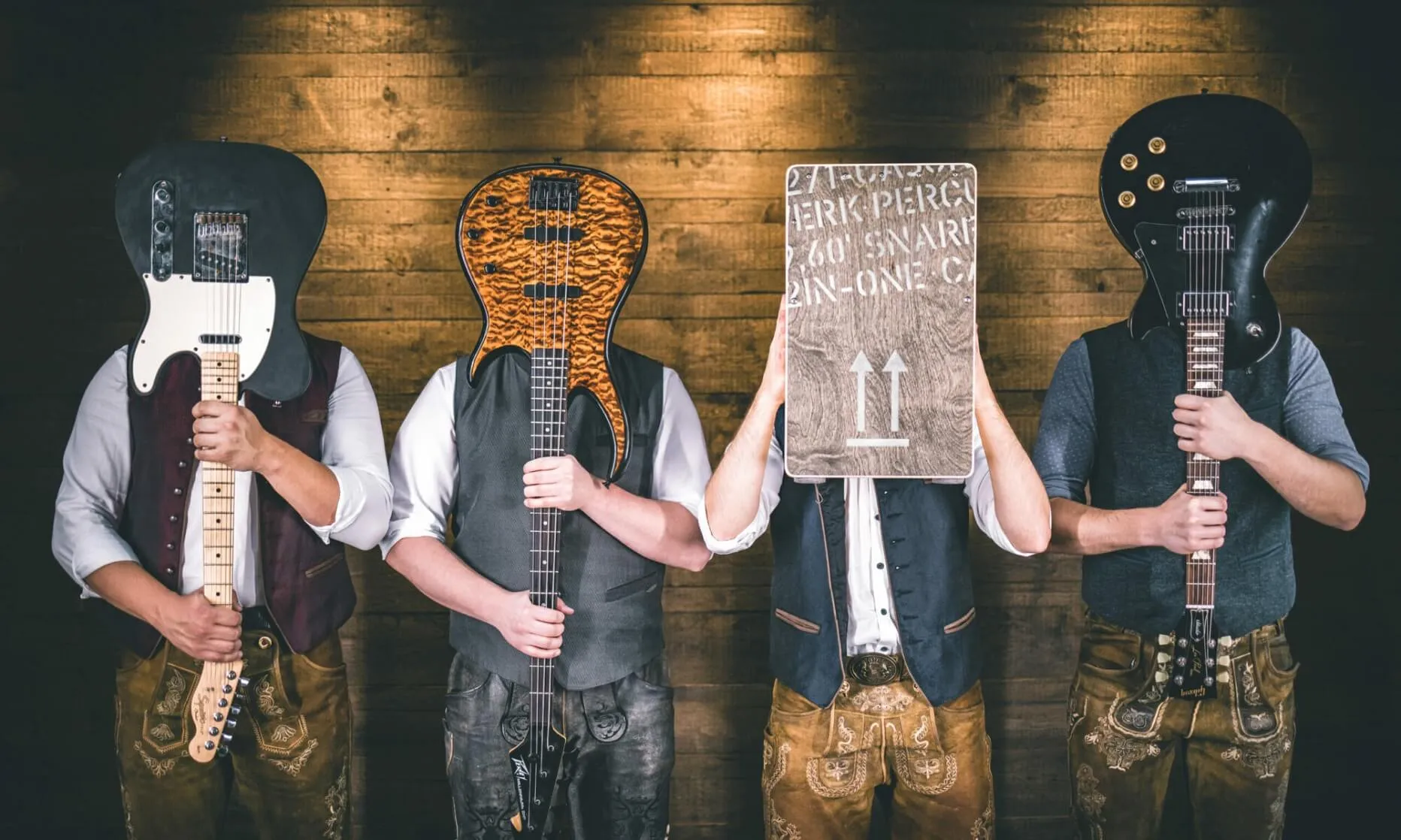 Die vier Musiker der bayrischen Partyband Campfire stehen mit ihren Instrumenten vor dem Kopf haltend vor einer rustikalen Holzwand.