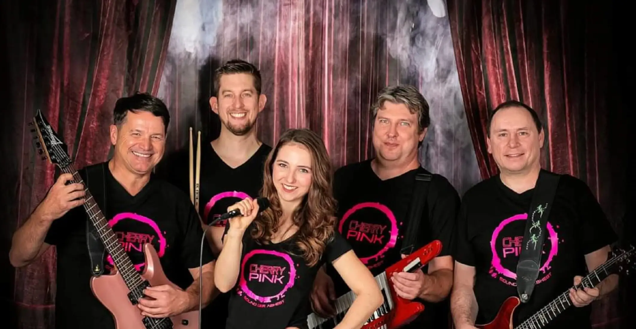 Die fünf Musiker der Partyband Cherry Pink mit ihren Instrumenten vor einer Fotoleinwand.