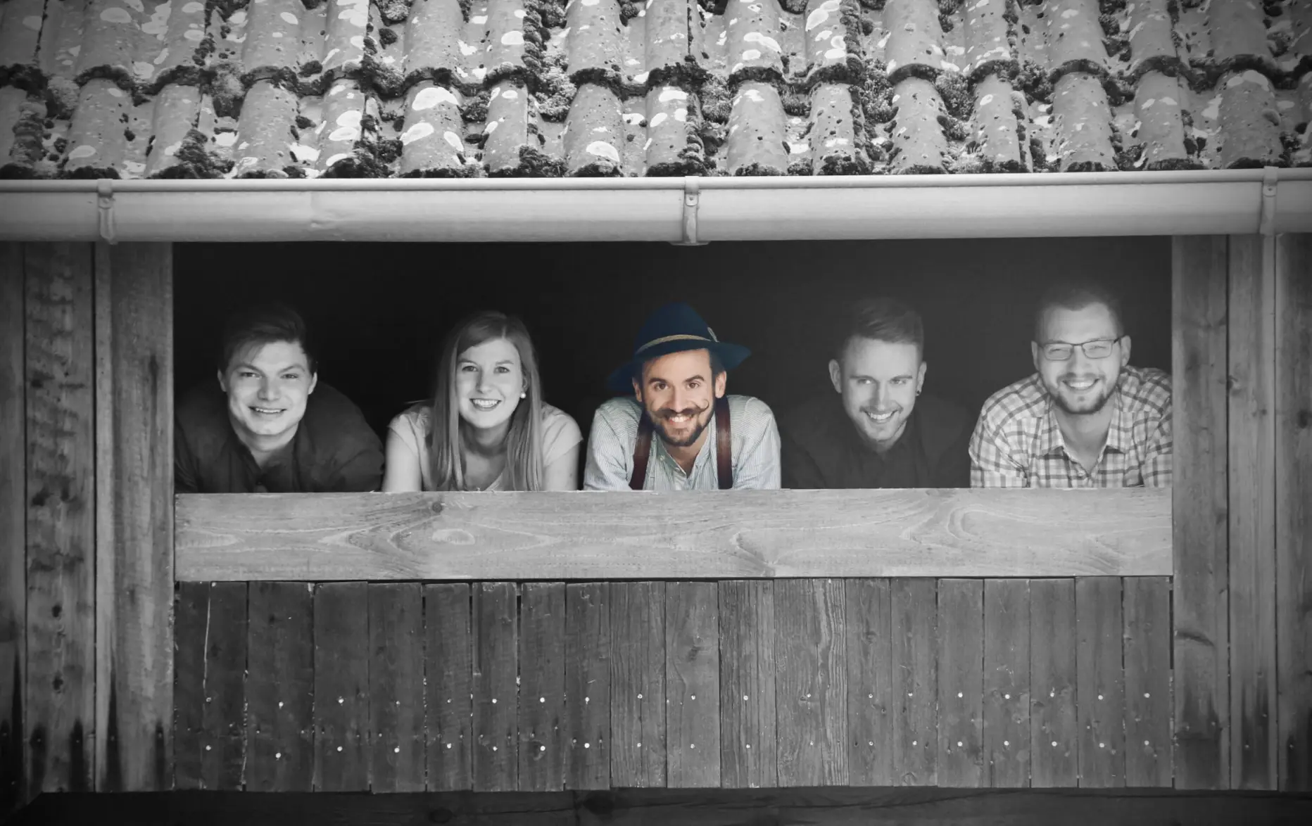 Die bayrische Partyband Grögötz Weißbir schaut von einem Holzbalkon nach unten.