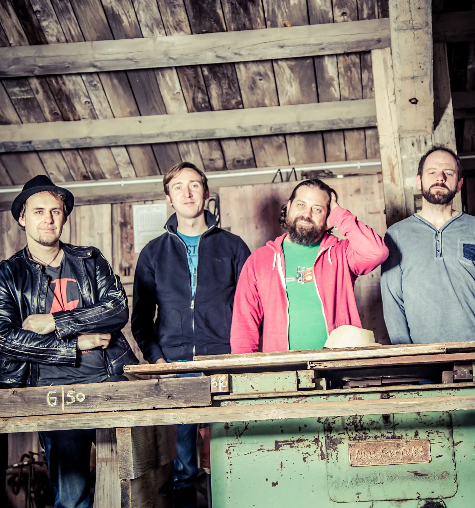 Die vier Musiker der Partyband Jive stehend in einem offenem Holzverschlag.