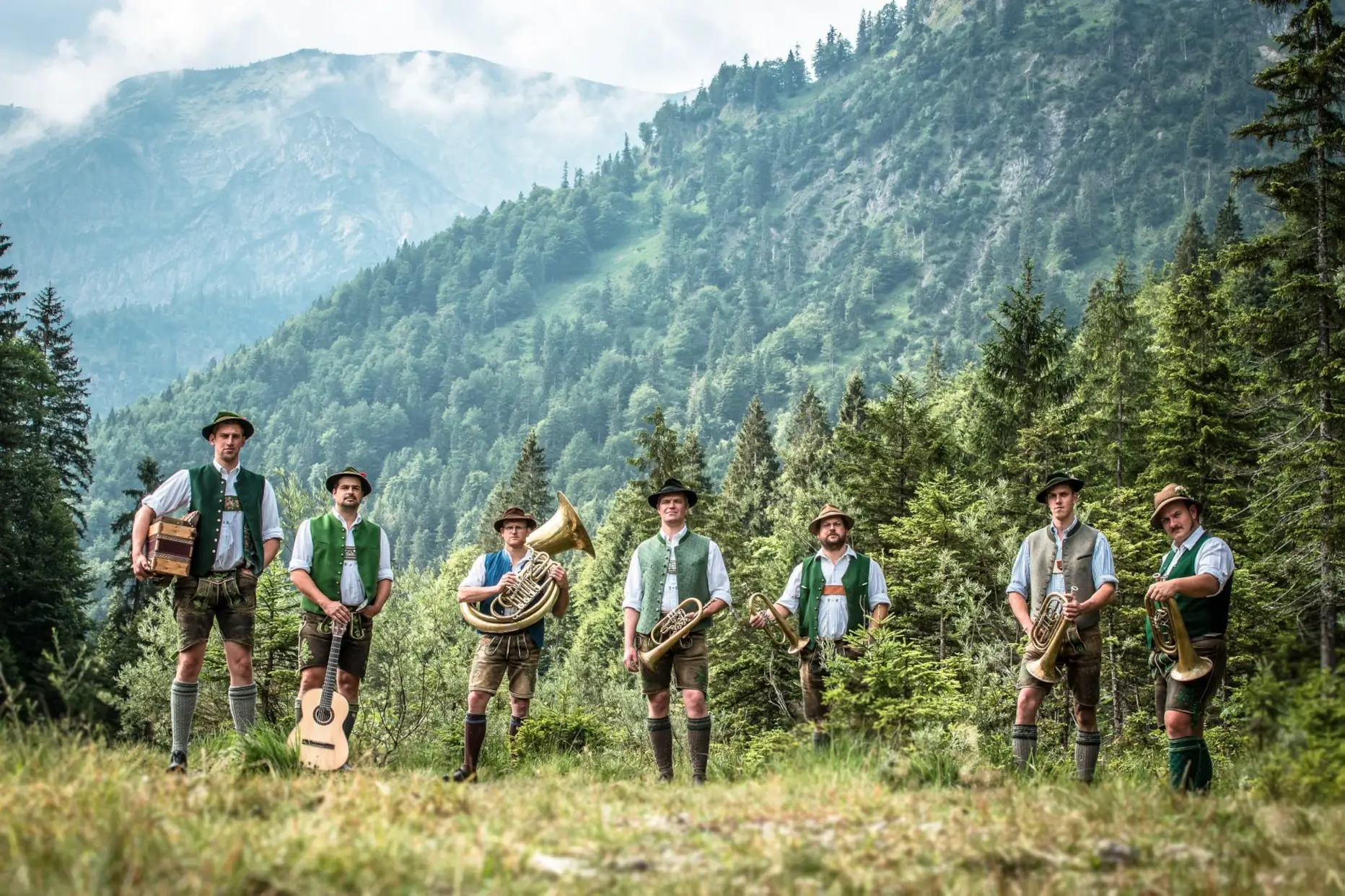 Die Tegernseer Tanzlmusi mit ihren Instrumenten vor einer alpenländischen Bergkulisse.