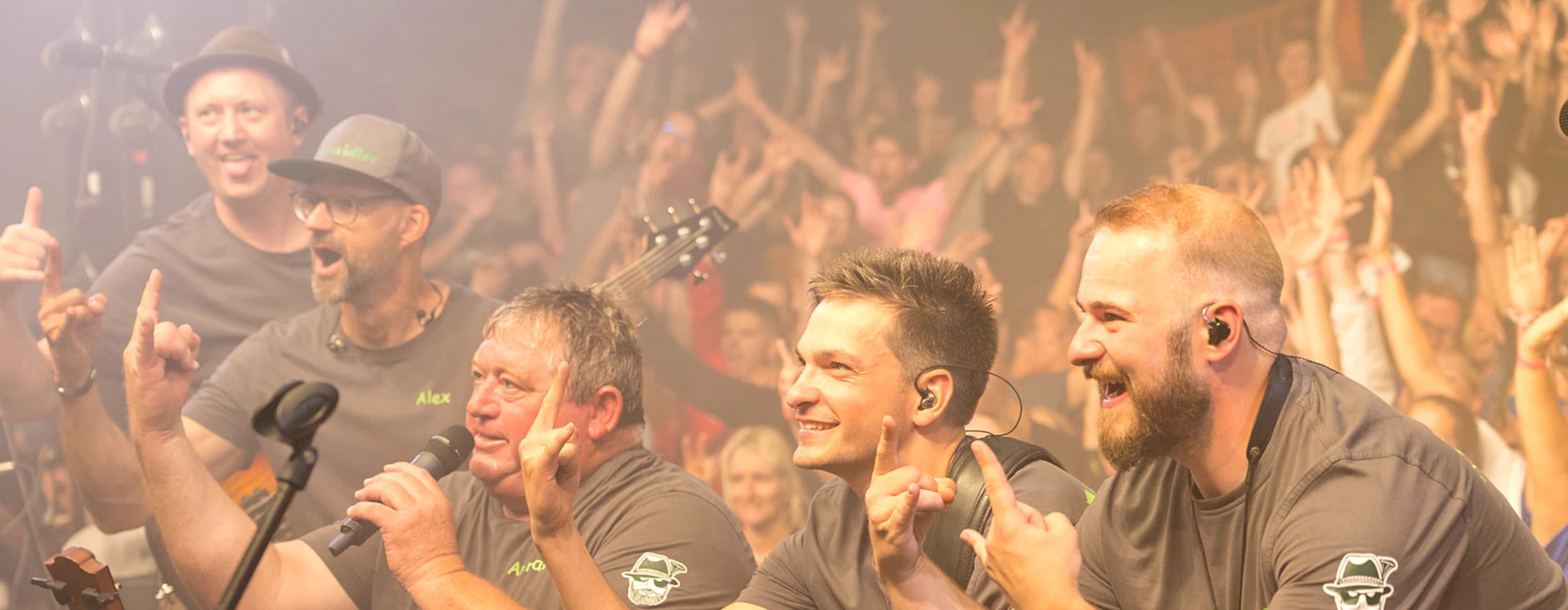 Urwaidler – die bayrische Partyband aus Rötz live auf einem Volksfest, fünf Musiker in grauen Band-Shirts feiern mit einem begeisterten Publikum in stimmungsvoller Atmosphäre.